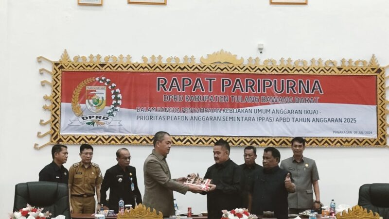 Sekdakab Tubaba Novriwan Jaya,  menyerahkan rancangan KUA PPAS tahun anggaran 2025 kepada Wakil Ketua I DPRD  Busroni, dalam rapat paripurna, Panaragan (9/7/2024). (Arie/NK)