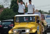 Pakal Calon Bupati dan Wakil Bupati Tubaba Novriwan Jaya-Nadirsyah (NoNa)  di atas kendaraan jeep terbuka terus melambaikan tangannya kepada masyarakat saat akan mendaftar ke KPU Tubaba, Rabu (28/08/2024)