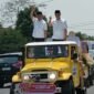 Pakal Calon Bupati dan Wakil Bupati Tubaba Novriwan Jaya-Nadirsyah (NoNa)  di atas kendaraan jeep terbuka terus melambaikan tangannya kepada masyarakat saat akan mendaftar ke KPU Tubaba, Rabu (28/08/2024)